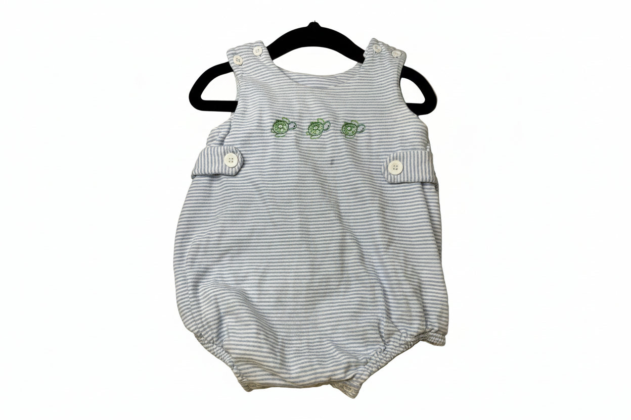 Striped baby romper with green turtles on a beige surface
