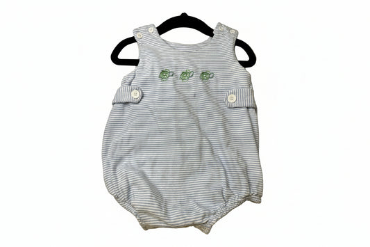 Striped baby romper with green turtles on a beige surface